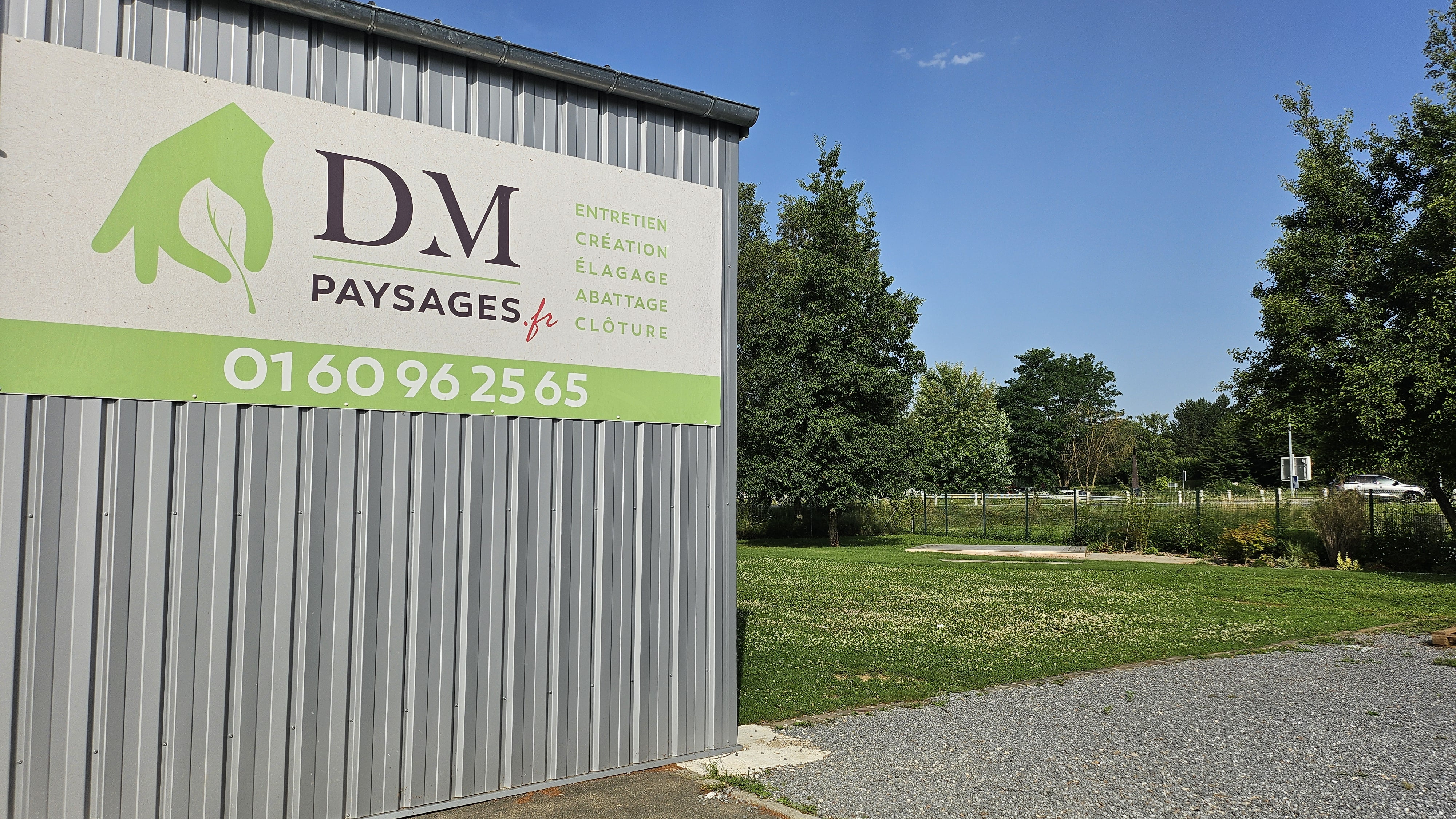 locaux de DM Paysages, entreprise de paysagistes, à gauche et de l'herbe à droite